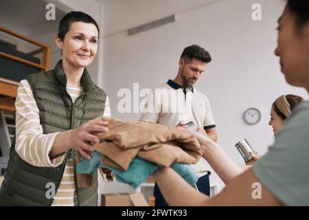 Portrait d'une femme mûre donnant des vêtements usagés aux bénévoles pendant l'événement d'aide et de dons, espace de copie Banque D'Images
