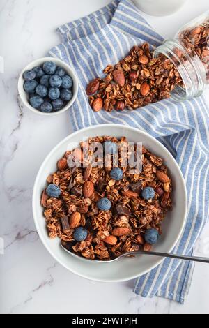 Granola maison, muesli avec morceaux de chocolat noir, noix et myrtilles dans un bol sur fond de marbre blanc. Petit déjeuner sain. Vue de dessus. Banque D'Images