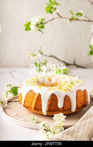Petit gâteau au citron frais maison décoré de glaçure blanche et de zeste sur fond de marbre blanc avec branches de prune en fleur. Banque D'Images