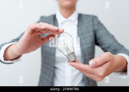Femme portant une ampoule à deux mains dans un ensemble formel présentant de nouvelles idées pour le projet, femme d'affaires tenant des ampoules dans les mains montrant tard Banque D'Images