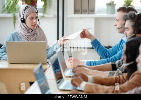 Une jeune femme arabe sérieuse dans le hijab donnant un script à appeler centrez vos collègues lorsqu'ils répondent aux appels Banque D'Images