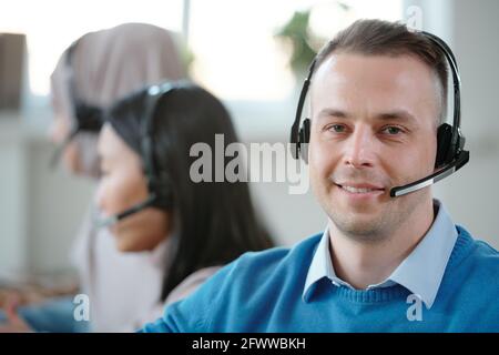 Portrait d'un très beau représentant du service clientèle de jeunes Caucasiens casque avec microphone placé contre vos collègues au travail Banque D'Images