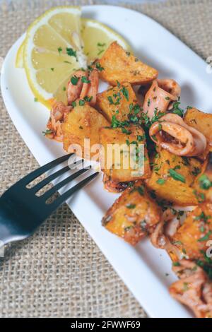 Apéritif ou tapa typiquement espagnol, calmar avec ail et pommes de terre, servi sur un plateau blanc allongé avec fond de citron et rustique. Traditionnel Banque D'Images