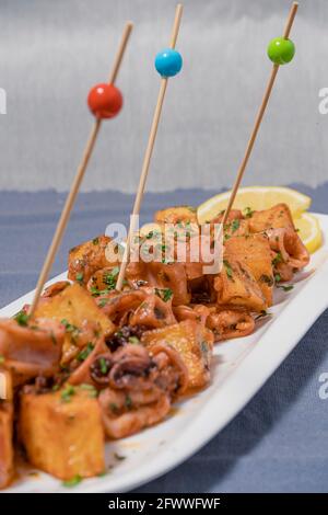 Apéritif ou tapa typiquement espagnol, calmar avec ail et pommes de terre, servi sur un plateau blanc allongé avec fond de citron et rustique. Traditionnel Banque D'Images