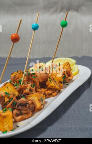 Apéritif ou tapa typiquement espagnol, calmar avec ail et pommes de terre, servi sur un plateau blanc allongé avec fond de citron et rustique. Traditionnel Banque D'Images