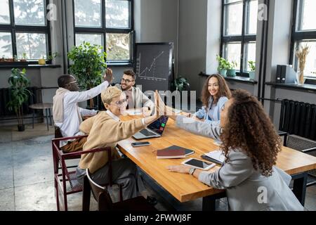 Des collègues joyeux se donnant un autre haut cinq sur la table dedans bureau Banque D'Images