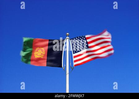 Les drapeaux afghans et américains flottent côte à côte dans des vents opposés sur un seul mât.Composite numérique. Banque D'Images