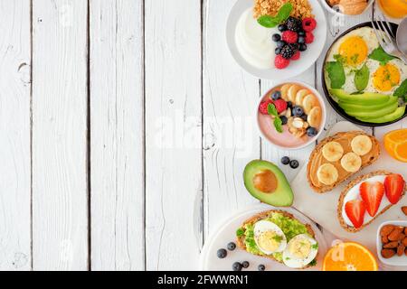Côté de la nourriture saine pour le petit déjeuner. Scène de table avec fruits, yaourt, smoothie, toasts nutritifs et poêle à oeufs. Vue ci-dessus sur un fond en bois blanc Banque D'Images