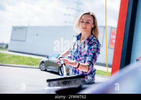 Femme dans une chemise à carreaux laver la voiture dans la station de lavage de voiture en libre-service. Banque D'Images