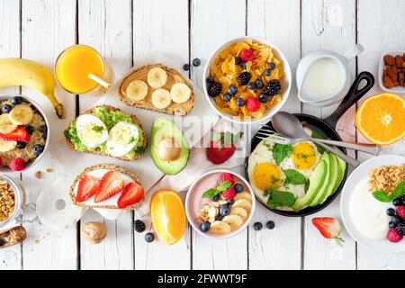 Table de petit déjeuner saine avec fruits, yaourts, flocons d'avoine, céréales, bol à smoothie, toasts nutritifs et poêle à œufs. Vue de dessus sur un dos en bois blanc Banque D'Images