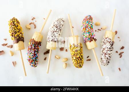 Pop de banane surgelé au chocolat avec noix, saupoudrer et noix de coco. Vue de dessus sur un fond en marbre blanc. Banque D'Images