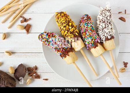 Pop de banane surgelé au chocolat avec saupoudrer, noix et noix de coco. Scène de table avec vue sur le dessus sur fond de bois. Banque D'Images