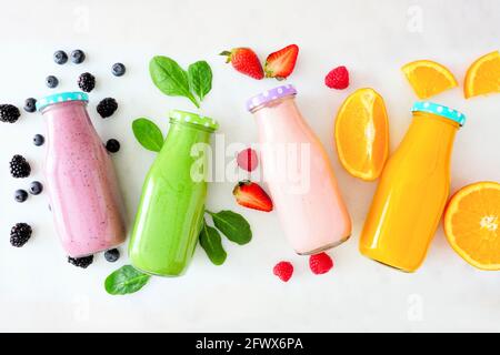 Assortiment de smoothies sains en bouteilles avec ingrédients. Vue du dessus, l'appartement est posé sur un fond en marbre blanc. Bleuet, vert, fraise et orange. Banque D'Images