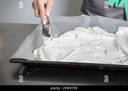 Femme mains chef répandre le mélange de protéines sur la surface du couvert de parchemin de cuisson. Processus de cuisson du gâteau Pavlova. Banque D'Images