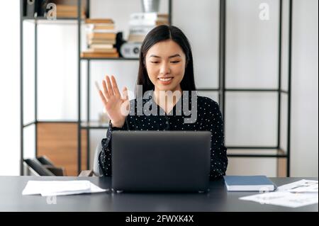 Sympathique mignon confiant jeune femme asiatique freelancer, directeur, pdg, assis au bureau à l'ordinateur portable, parler par appel vidéo avec le client ou les employés, discuter de la stratégie d'entreprise, de la main de la main, sourire Banque D'Images