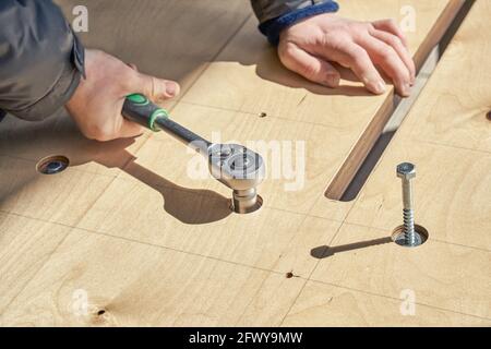 Un artisan qualifié assemble les vis tournantes de la grande table à manger en bois avec clé à l'extérieur, vue de très près par temps ensoleillé Banque D'Images