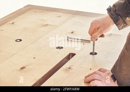 Un artisan qualifié assemble les boulons de rotation de la grande table à manger en bois avec la main à l'extérieur sur une vue de très près par temps ensoleillé Banque D'Images