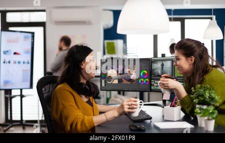 Une équipe de vidéastes qui prennent une pause-travail en discutant et en riant, en buvant du café dans une application de montage vidéo sur un pc installé dans une entreprise de multimédia numérique. Les femmes créatives prosessant le montage de film Banque D'Images