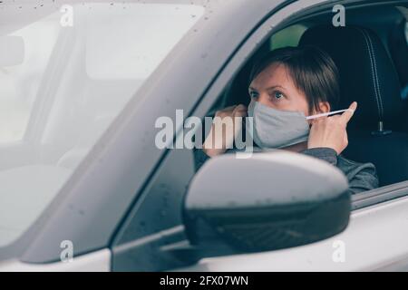 Femme portant un masque de protection en voiture pendant les pandémies de Covid-19, regardant le miroir, foyer sélectif Banque D'Images