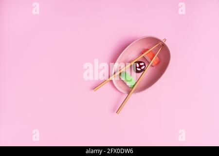Vue imprenable sur les délicieux sushis colorés servis en céramique plaque avec baguettes en bois sur fond rose Banque D'Images