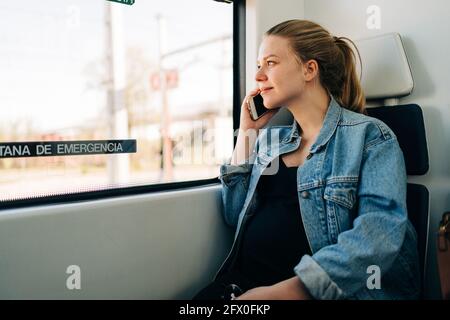 Vue latérale d'une femme anonyme assise sur la plage près de la mer et écouter de la musique sur des écouteurs et sur un téléphone portable Banque D'Images