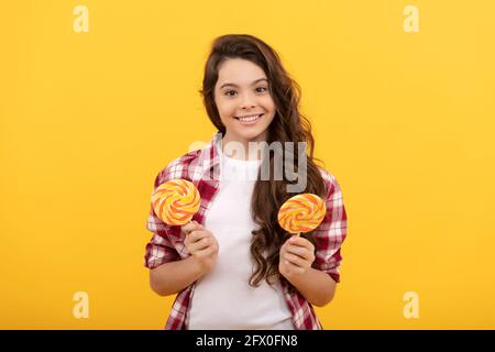 bonne fille de l'adolescence avec les cheveux bouclés tenir la bonbon de caramel de lollipop sur fond jaune, boutique de caramel. Banque D'Images