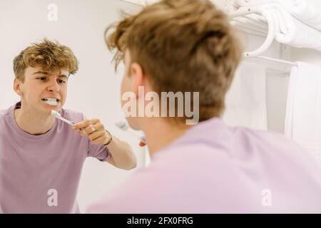 Vue latérale d'un barkeeper sérieux dans des lunettes de vue qui versent de la bière verre pendant qu'il travaille en bar pendant une pandémie de coronavirus Banque D'Images