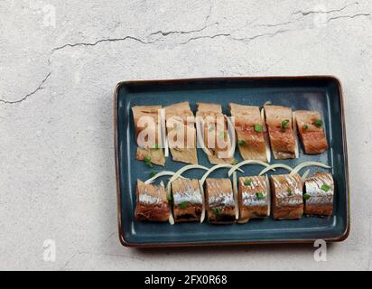 Filet de hareng salé avec oignons sur une plaque rectangulaire sur fond gris clair. Vue de dessus, plan d'appartement Banque D'Images