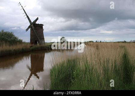 Paysage de l'ancienne pompe de moulin à vent de brique avec des voiles de bois se reflètent dans l'eau de rivière de Norfolk Broads Horsey East Anglia Angleterre par la banque de roseaux herbeux Banque D'Images