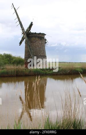 Paysage de l'ancienne pompe de moulin à vent de brique avec des voiles de bois se reflètent dans l'eau de rivière de Norfolk Broads Horsey East Anglia Angleterre par la banque de roseaux herbeux Banque D'Images