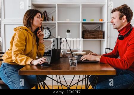 Homme et femme travaillant à la maison à la table en face l'un de l'autre. Banque D'Images