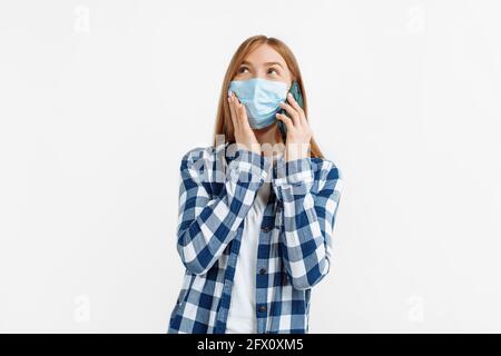 Jeune femme gaie dans un masque médical parlant au téléphone, tenez le smartphone près de l'oreille, sur un arrière-plan blanc isolé Banque D'Images