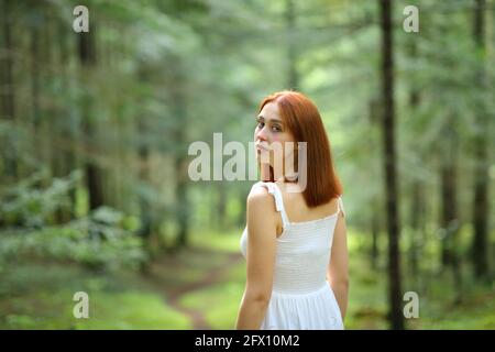 Belle femme marchant seule dans une forêt verte regardant caméra au printemps Banque D'Images