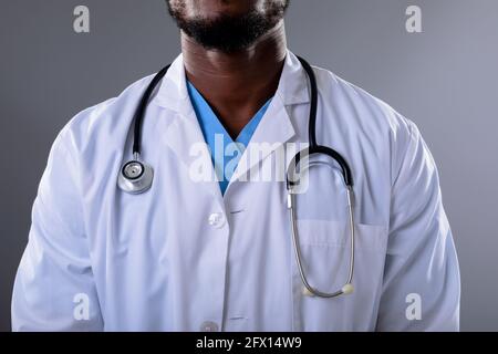 Section médiane d'un homme afro-américain portant un stéthoscope contre arrière-plan gris Banque D'Images