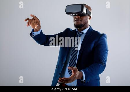 Un homme d'affaires afro-américain portant un casque vr se faisant des gestes sur fond gris Banque D'Images