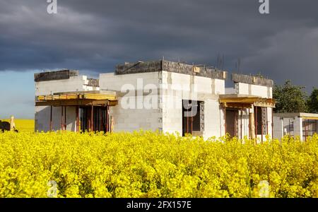 Maison familiale rurale en construction avec champ de colza en premier plan et nuages orageux en arrière-plan. Banque D'Images