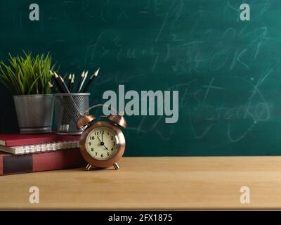 Concept d'éducation, table d'étude avec horloge, papeterie, pot de plantes et espace de copie sur table en bois avec fond de mur de tableau noir Banque D'Images