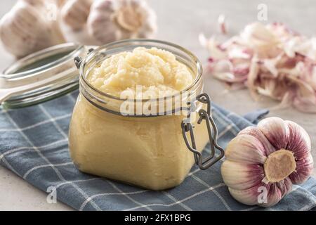 Pâte d'ail aromatique dans un pot en verre posé sur un chiffon de cuisine rustique avec des bulbes et des clous de girofle pelés. Banque D'Images