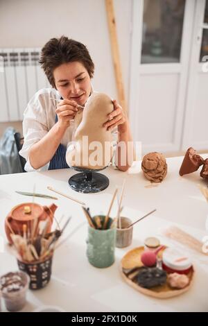 Potter atteignant la tête du modèle d'argile avec outil de sculpture Banque D'Images