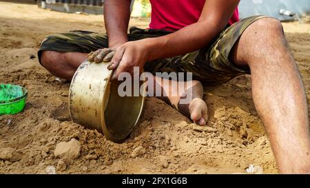 Homme indien non identifié nettoyant pot en laiton avec du sol pur. Paysage rural indien. Banque D'Images