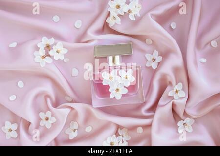 Bouteille en verre de parfum de luxe aromatique sur un tissu en soie rose doux avec fleurs de la branche. Emballage minimaliste, marquage. Floral Banque D'Images