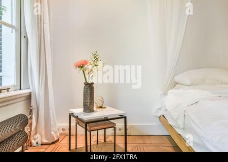 Intérieur d'une chambre blanche spacieuse avec lit queen size auvent blanc et porte ouverte menant au jardin vert Banque D'Images