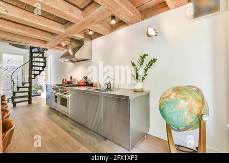 Armoires en chrome brillant et appareils de cuisine moderne dans le pays maison avec plafond à poutres apparentes et escalier en colimaçon Banque D'Images