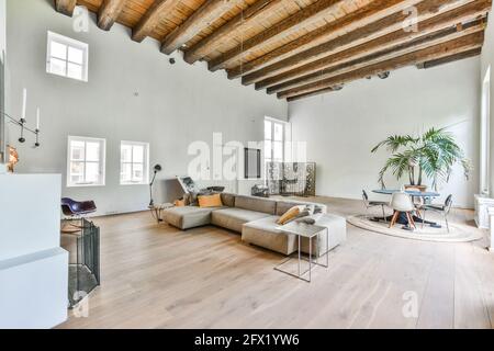 Grande chambre avec de hauts plafonds à poutres apparentes et mobilier gris canapé et éléments de design artistique dans un style minimaliste Banque D'Images