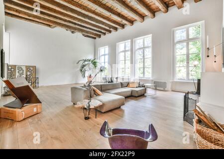 Grande chambre avec de hauts plafonds à poutres apparentes et mobilier gris canapé et éléments de design artistique dans un style minimaliste Banque D'Images