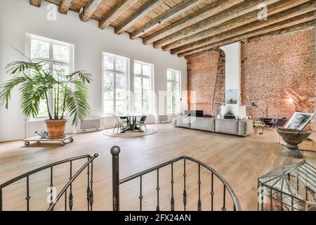 Grande chambre avec de hauts plafonds à poutres apparentes et mobilier gris canapé et éléments de design artistique dans un style minimaliste Banque D'Images