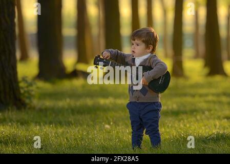 Little Boy jouer guitare dans la forêt au coucher du soleil Banque D'Images