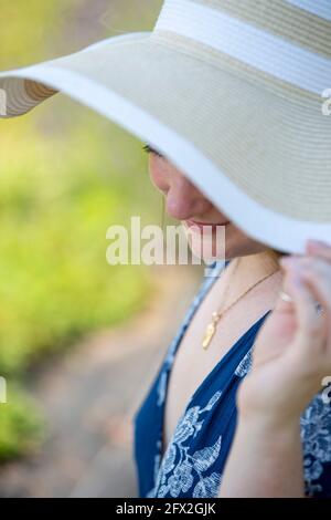 Belle jeune femme portant un chapeau de soleil de disquette se trouve dans un champ de lavande frais. Fleurs des prés, campagne Paysage bokeh arrière-plan Banque D'Images