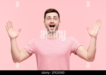 Portrait d'homme excité surpris avec les bras levés sur fond rose. Émotions, succès, concept gagnant Banque D'Images