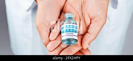 gros plan d'un professionnel de la santé, portant une blouse de laboratoire blanche, avec une bouteille de vaccin covid-19 simulée dans ses mains, dans un format panoramique à utiliser comme w Banque D'Images